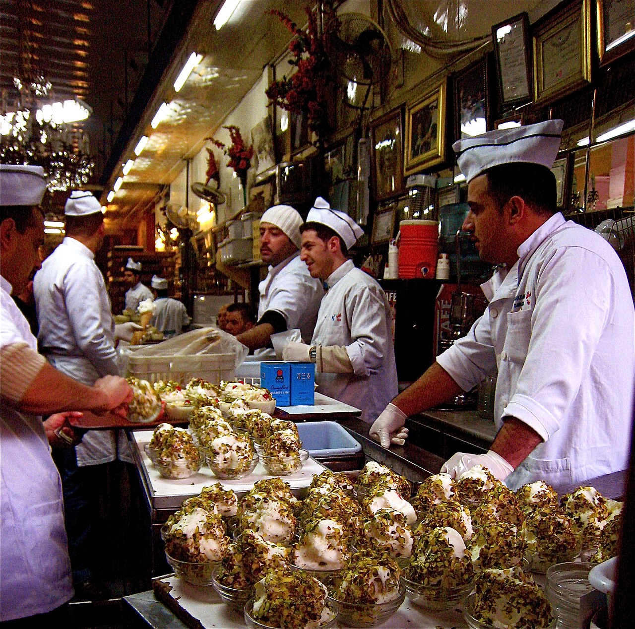 The interior of Bakdash ice cream parlour in Damascus, with staff in white coats serving booza topped with pistachio