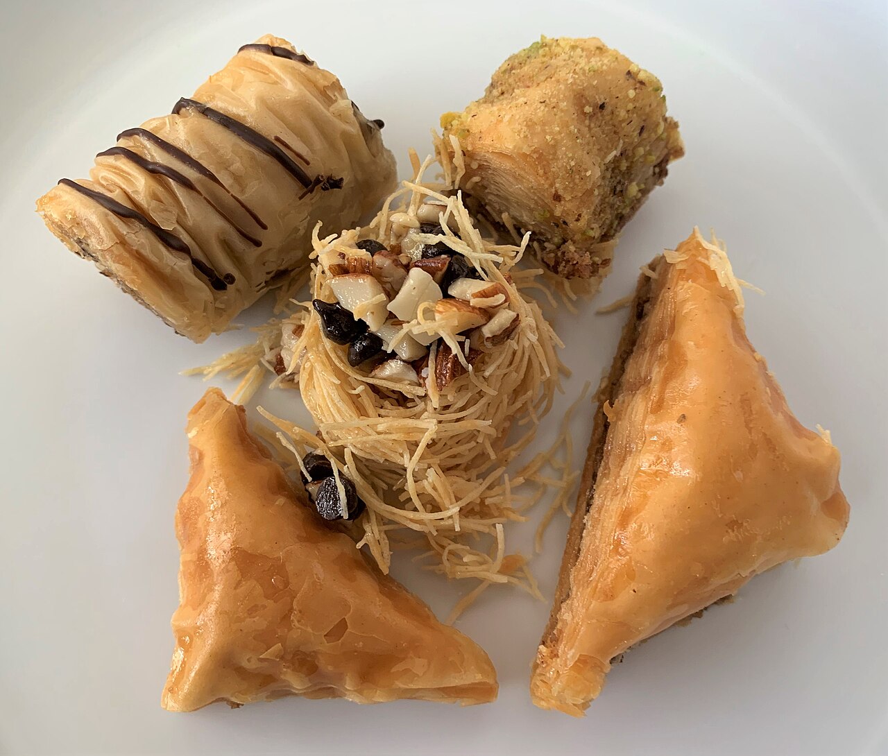 An assortment of baklava pieces including triangles and a shredded-pastry nest filled with nuts