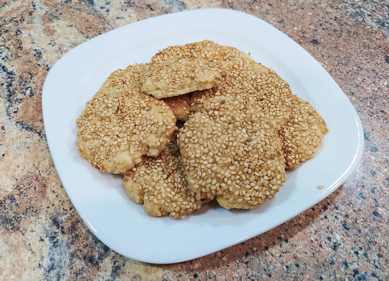A plate of flat round barazek cookies thickly coated in sesame seeds