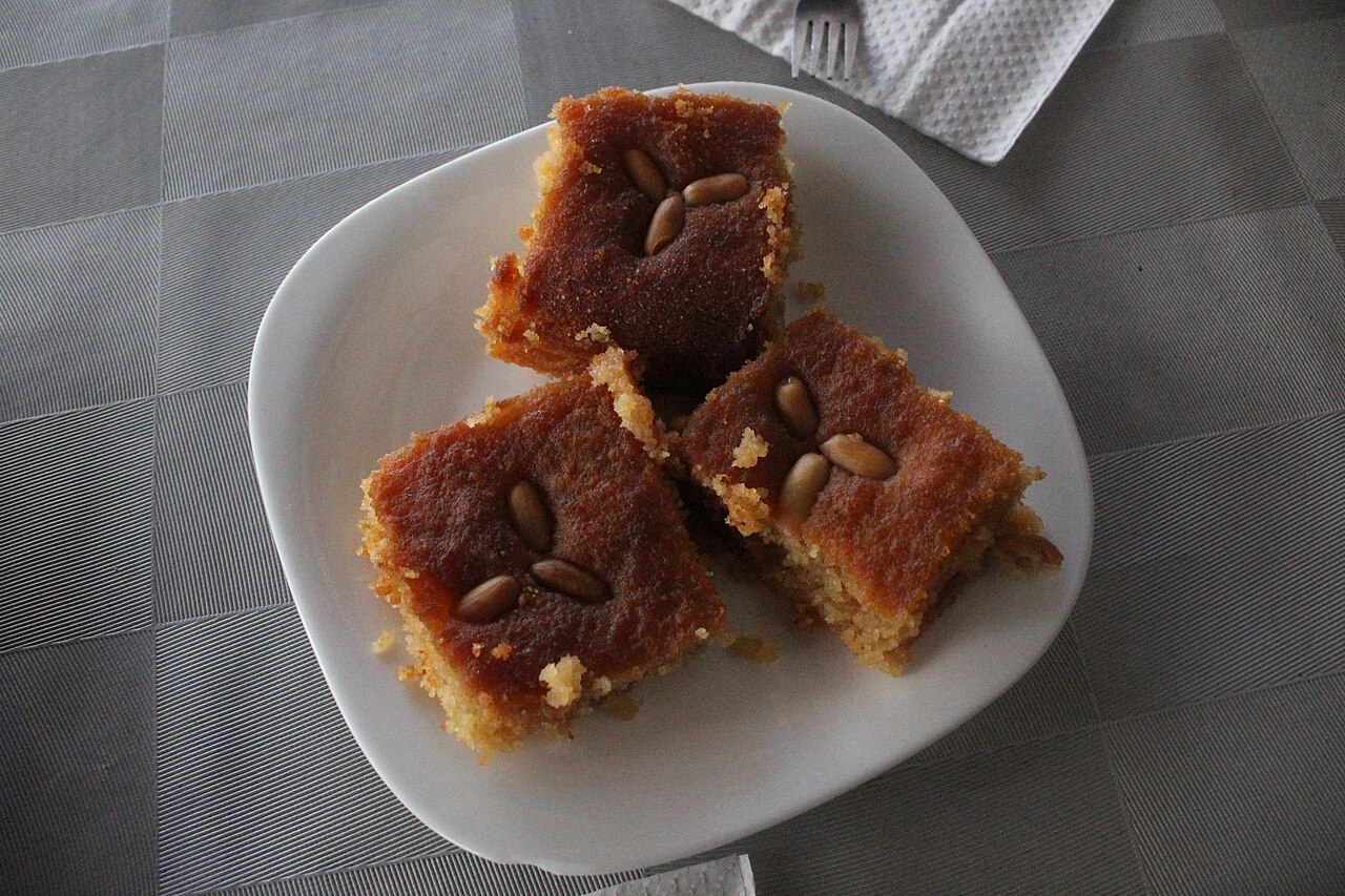 Three squares of basbousa semolina cake topped with pine nuts
