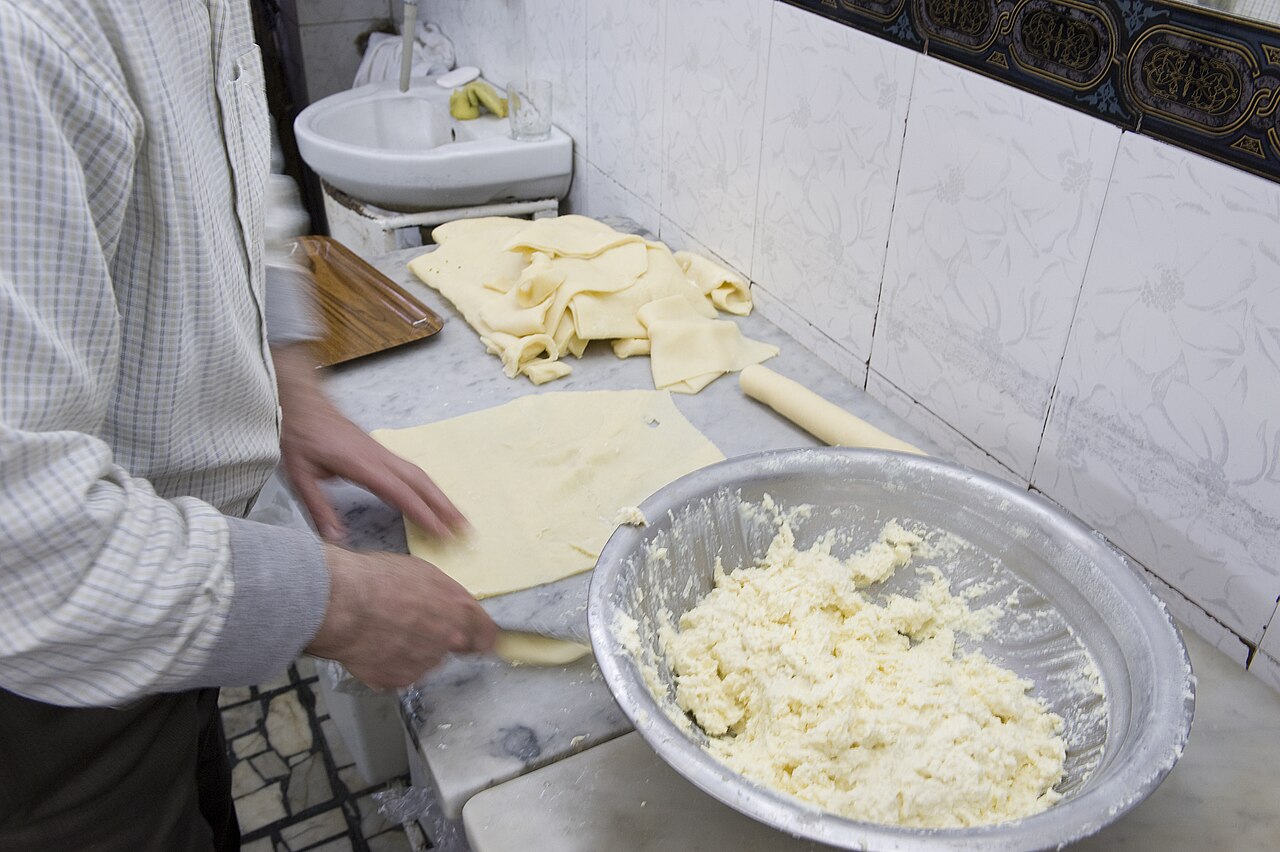 A confectioner in Hama rolling out dough beside a bowl of white cheese filling