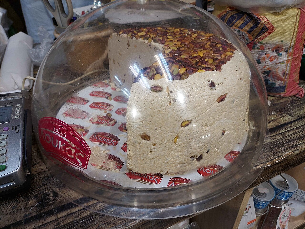 A block of pale tahini halva topped with pistachios under a glass dome