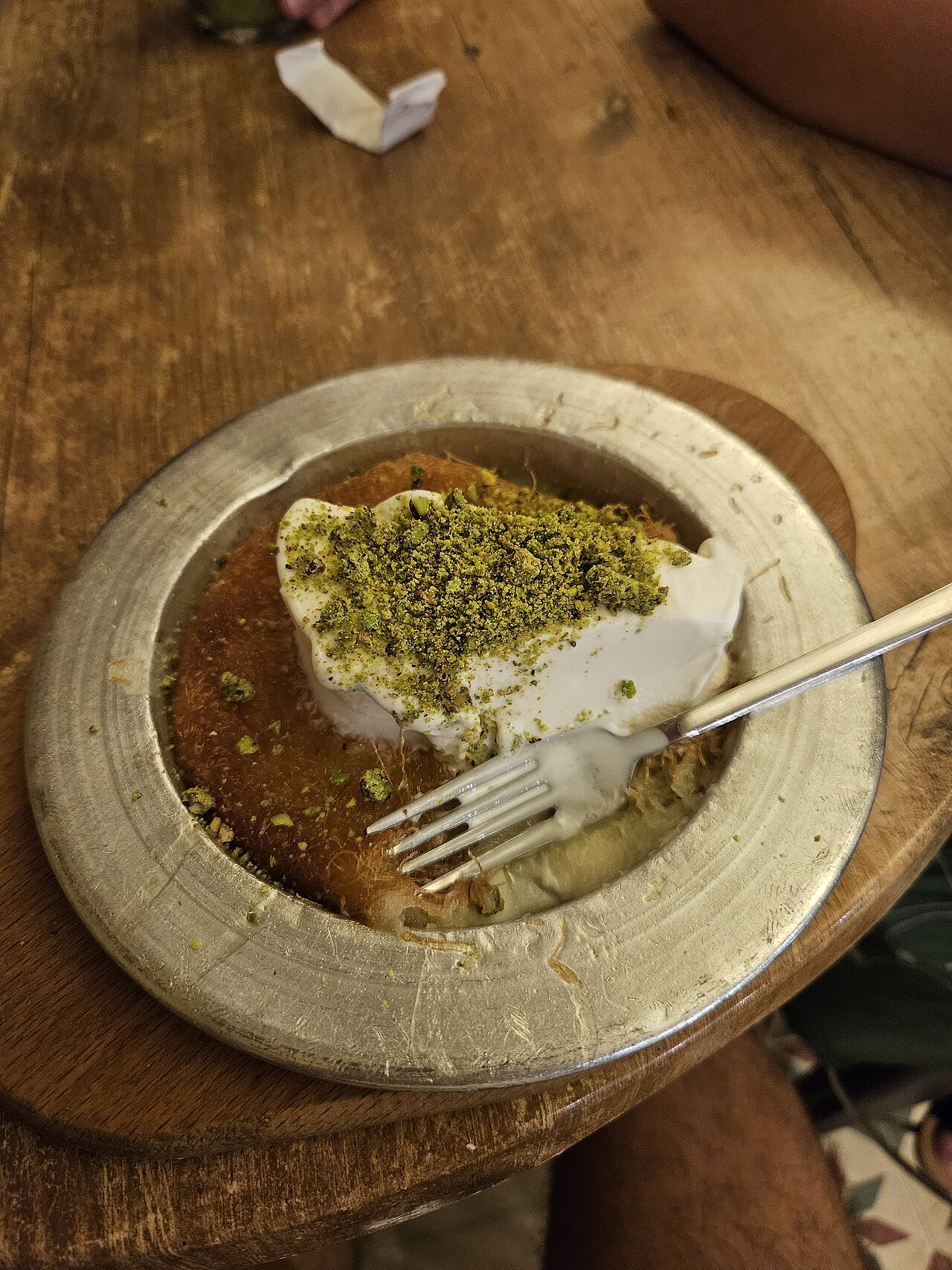 A portion of kanafeh with a layer of white kaymak and a dusting of green pistachio