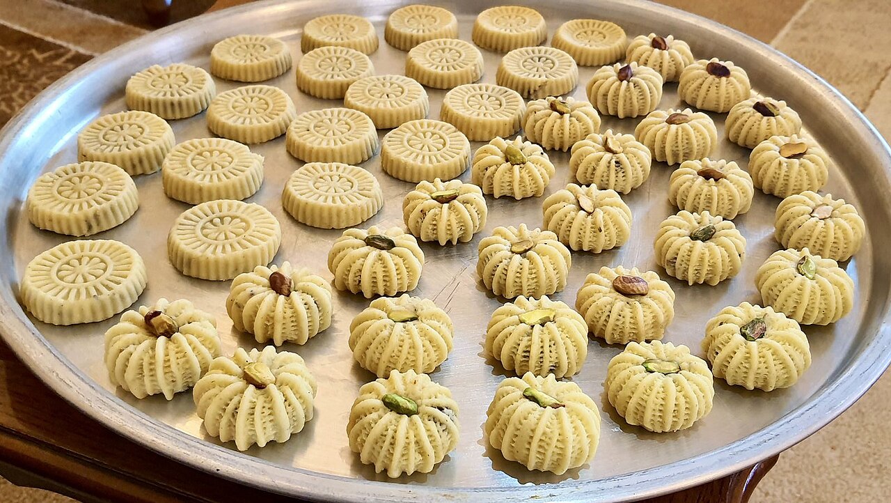 A tray of maamoul cookies pressed in decorative wooden moulds, some topped with pistachio