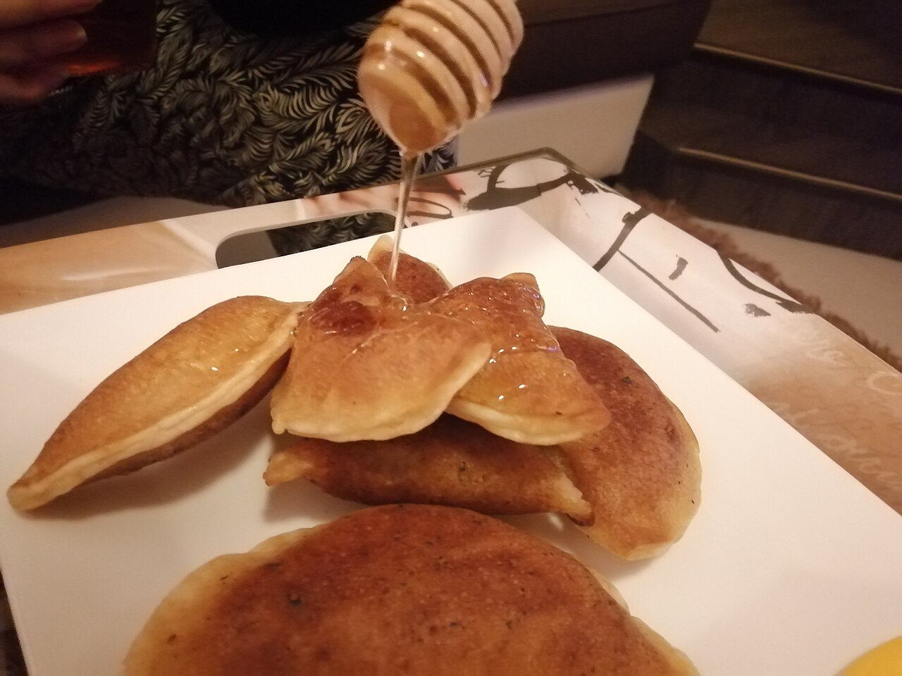 Folded qatayef pancakes on a plate with honey being drizzled over them
