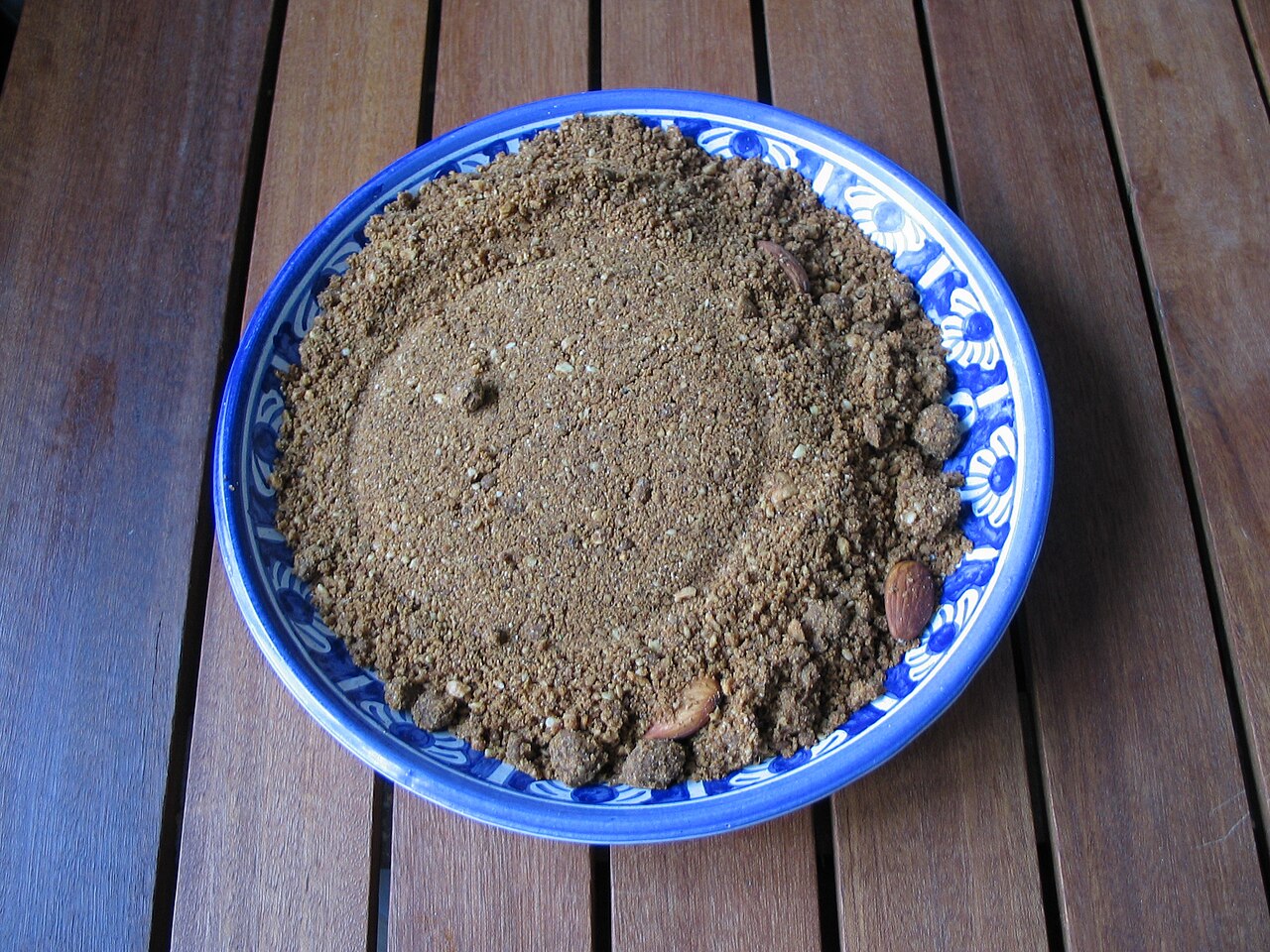 A blue and white bowl of dark golden sfouf semolina cake topped with almonds