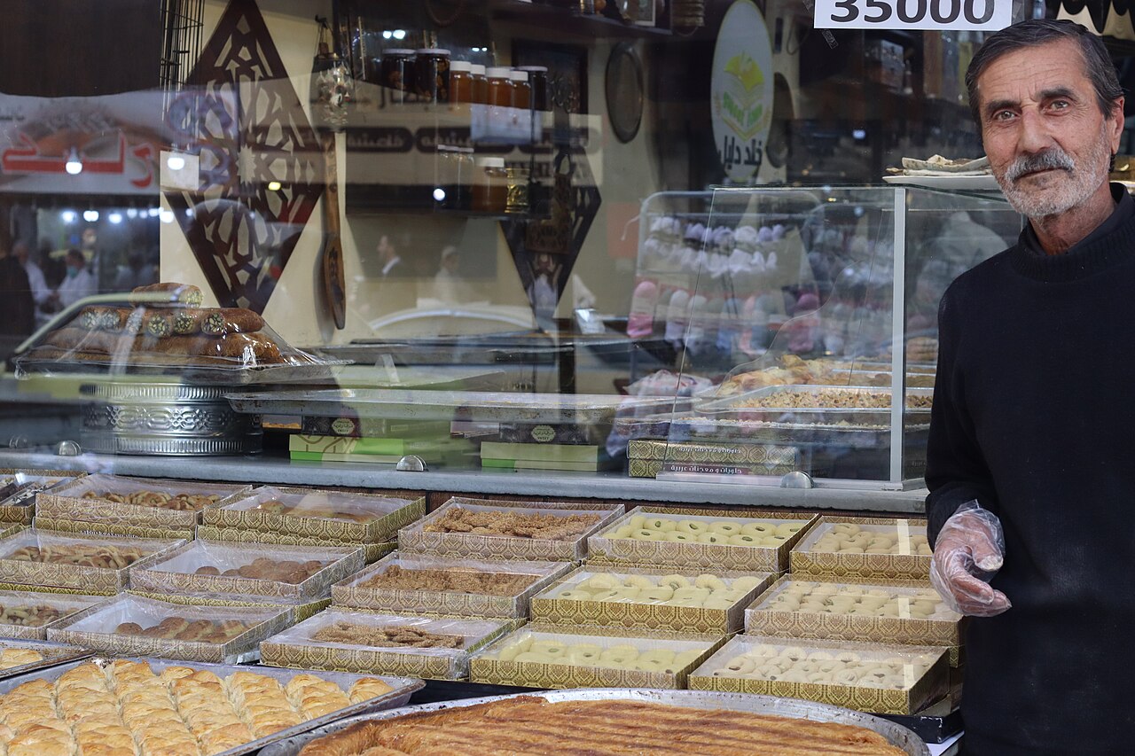A Syrian pastry shop counter lined with trays of maamoul and boxes of assorted sweets
